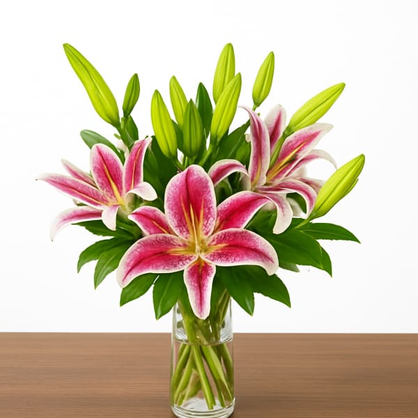 Pink and white lilies with green buds arranged in a clear glass vase on a wooden surface