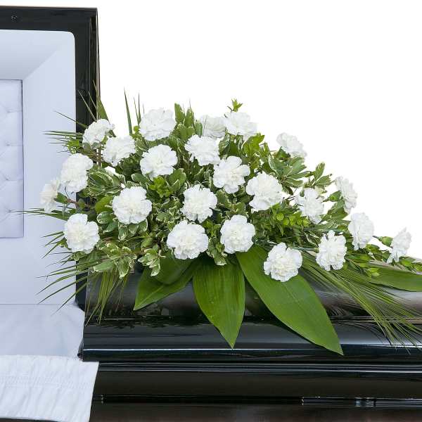 White carnation casket spray with broad green foliage on a black casket beside a white interior lining.