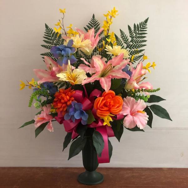 Tall silk arrangement of colorful mixed flowers in a dark green pedestal vase