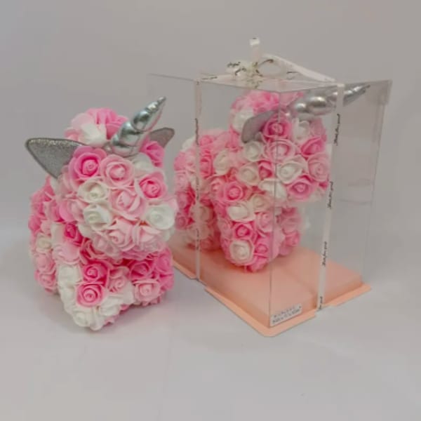 Pink and white rose-covered unicorn figurine with silver horn, one displayed in a clear gift box.