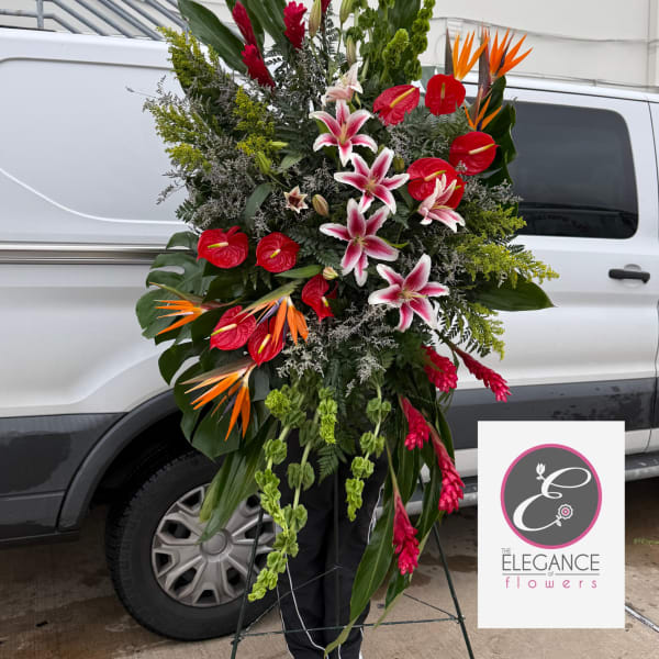 Tall standing spray with pink lilies, red tropical flowers, and orange bird-of-paradise on a metal easel.
