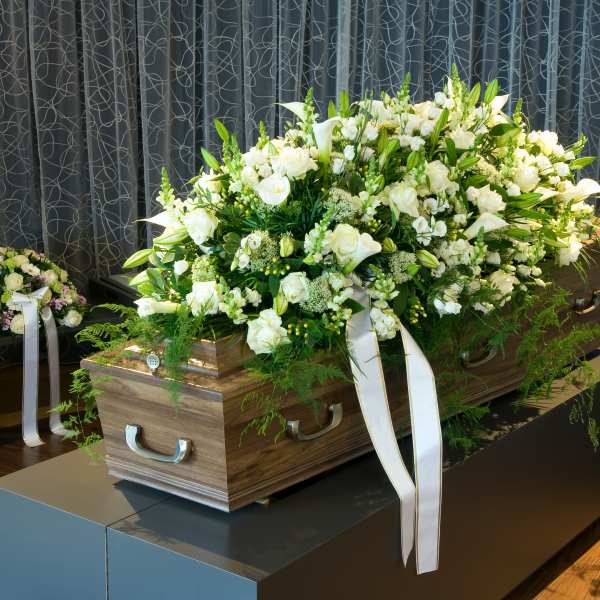 Large white and green casket spray of roses and lilies with ribbons on a wooden casket in a funeral setting