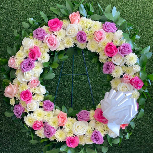 Circular floral wreath of pink, purple, and white roses with a white bow