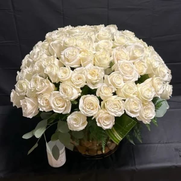Large dome of cream roses in a clear vase with a white candle on a black background