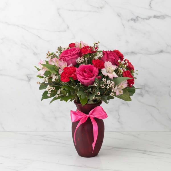 Pink and red flower arrangement in a burgundy vase with a pink ribbon
