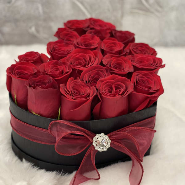 Heart-shaped black box filled with red roses and tied with a red bow and jewel accent