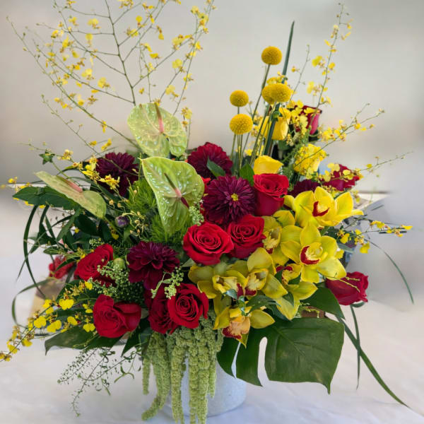 Mixed bouquet with red roses, yellow orchids, and burgundy blooms in a white vase