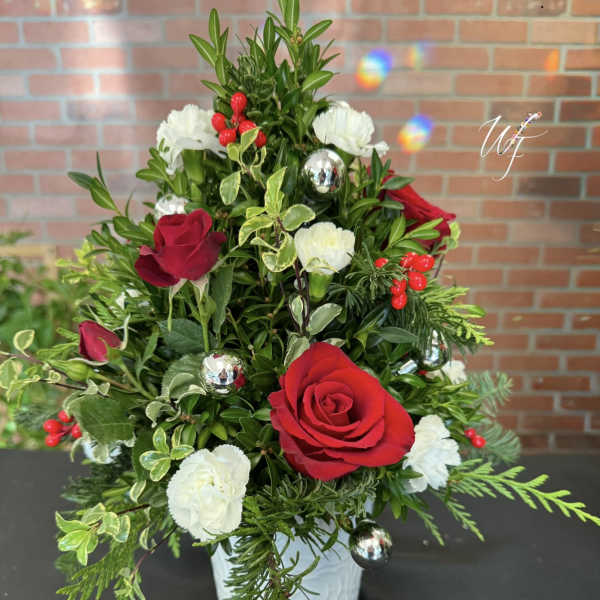 Red and white roses arranged in a white vase with holiday ornaments