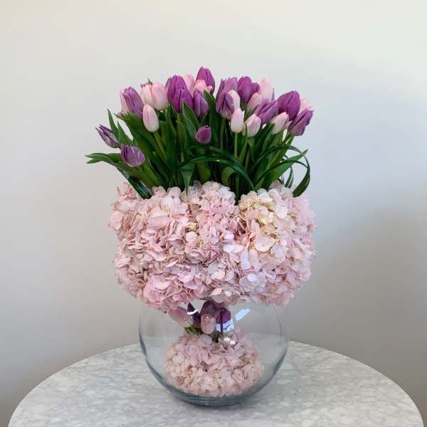 Pink hydrangeas and purple tulips arranged in a clear glass vase