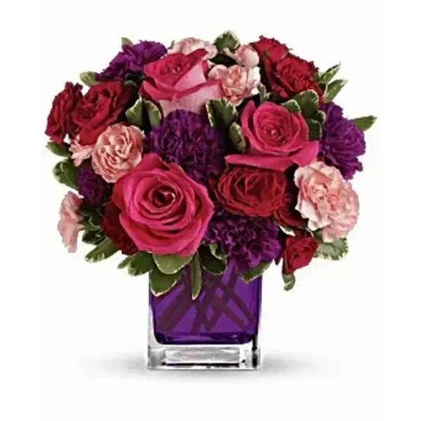 Compact bouquet of pink and red roses with carnations in a purple glass cube vase