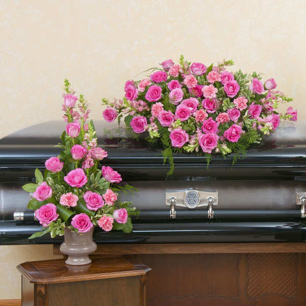 Pink rose and carnation casket spray with two matching standing arrangements on a dark casket