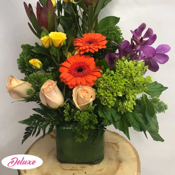 Mixed bouquet in a green vase with orange gerberas, roses, and purple orchids