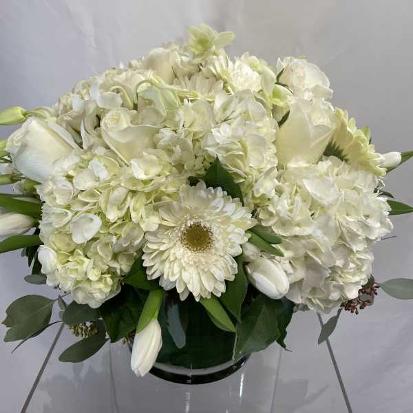 White floral arrangement in a glass vase with hydrangeas, roses, and daisies