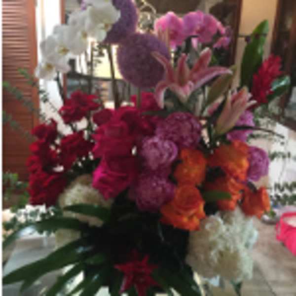 Tall mixed arrangement with red and pink roses, orange flowers, lilies, orchids, and white blooms.
