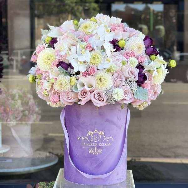 Large pastel bouquet of roses, orchids, and mums in a purple hatbox