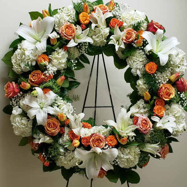 Standing wreath of white lilies, hydrangeas, and orange roses on a metal easel
