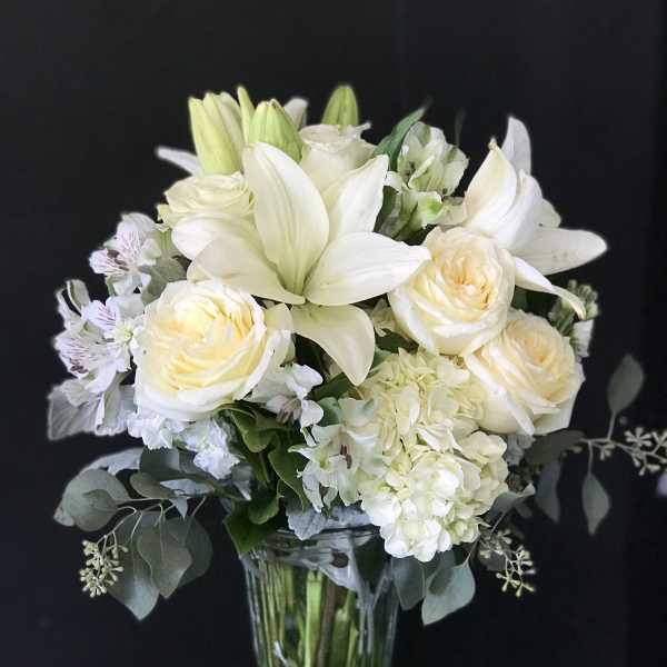White lilies and cream roses arranged in a clear glass vase