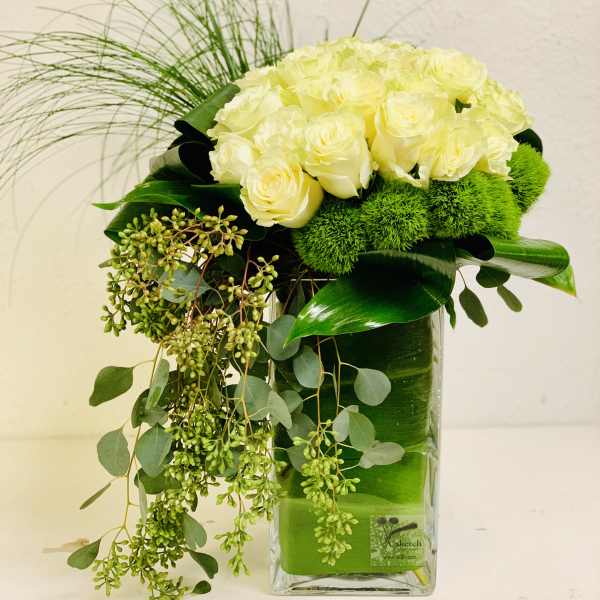 White roses arranged in a clear rectangular vase with trailing greenery
