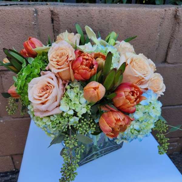 Low arrangement of peach roses and orange tulips with green hydrangeas in a clear glass vase