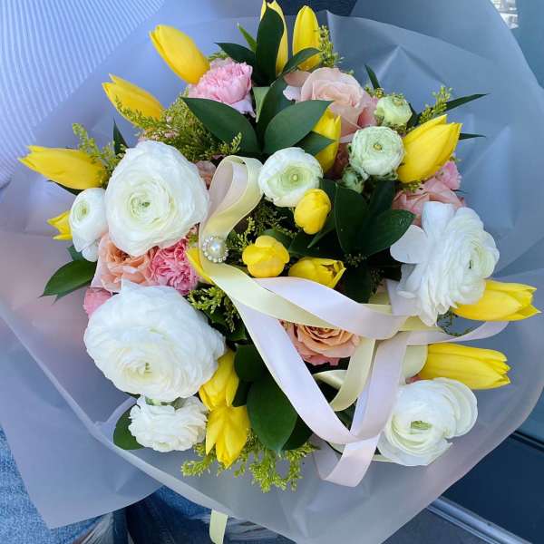 Bouquet of yellow tulips, white ranunculus, and pale pink roses with ribbon