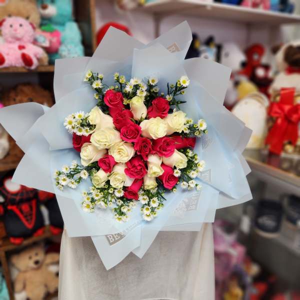 Bouquet of pink and white roses with small white daisies in pale blue wrap