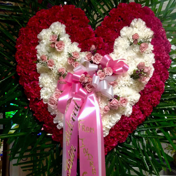 Heart-shaped floral tribute with pink and white flowers and a pink ribbon bow