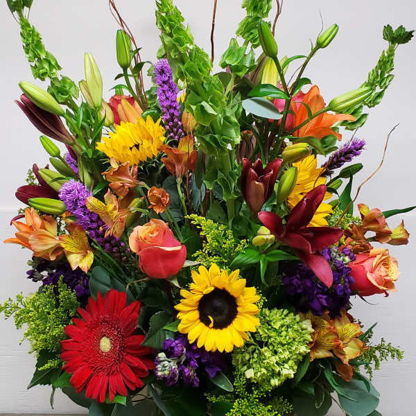 Tall mixed arrangement with sunflowers, lilies, roses, gerbera and bells of Ireland in a clear glass vase