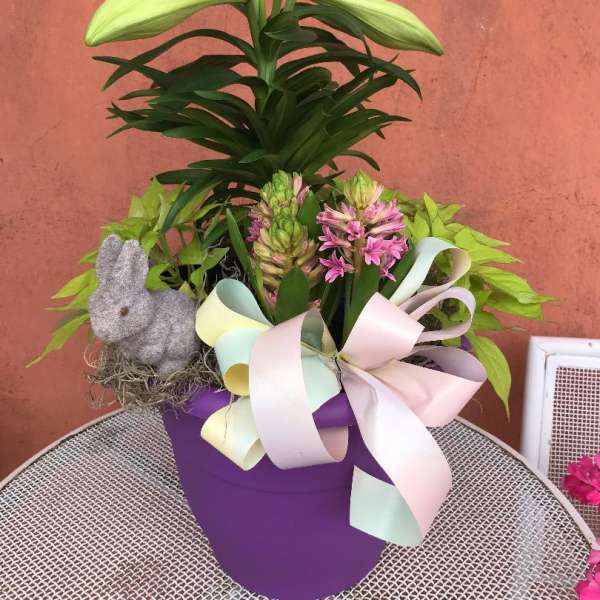 Potted lily and pink hyacinths in a purple container with pastel bow and bunny figurine.
