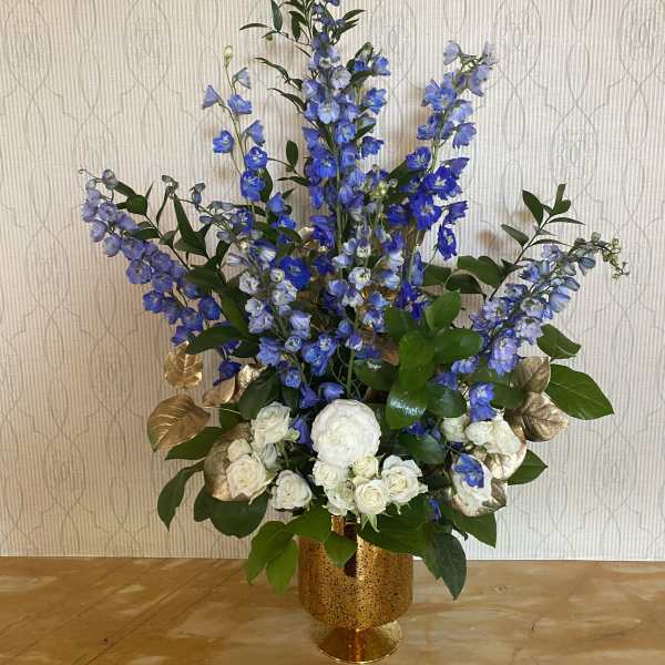 Tall blue and white floral arrangement in a gold vase