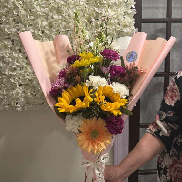 Mixed bouquet with sunflowers, gerbera daisies, and carnations in pink wrap