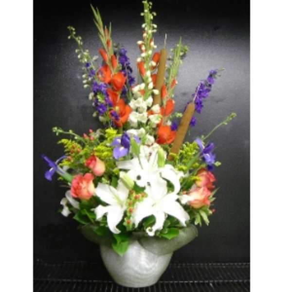 Tall mixed arrangement of white lilies, orange and purple flowers in a white vase