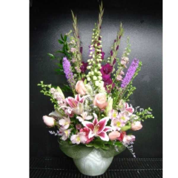Tall pink and purple mixed flower arrangement with lilies and roses in a white ceramic vase