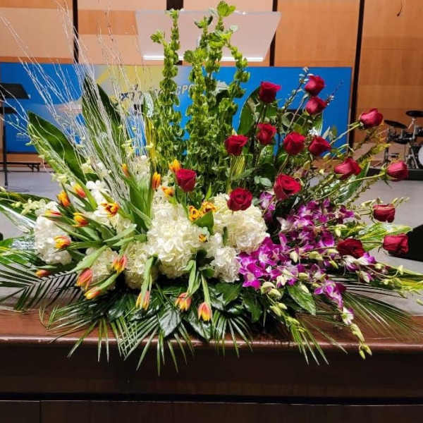 Large altar-style arrangement with red roses, white hydrangeas, orchids, tulips, and tall green spikes.