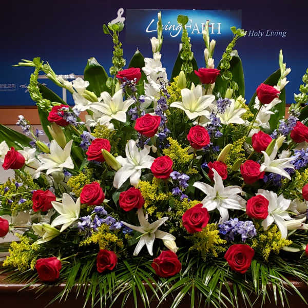 Large altar arrangement of red roses, white lilies, and blue flowers in a fan shape on a stage