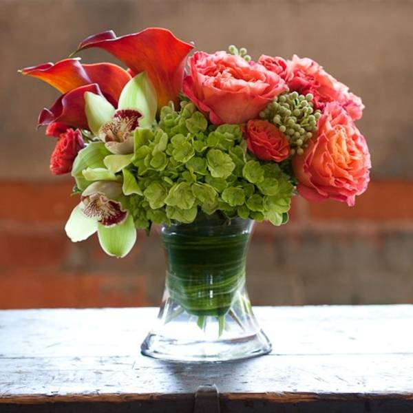 Bouquet of coral roses, green hydrangea, and calla lilies in a glass vase