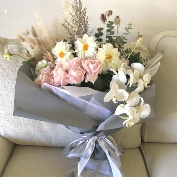 Bouquet of pink roses, white flowers, and dried grasses wrapped in gray paper