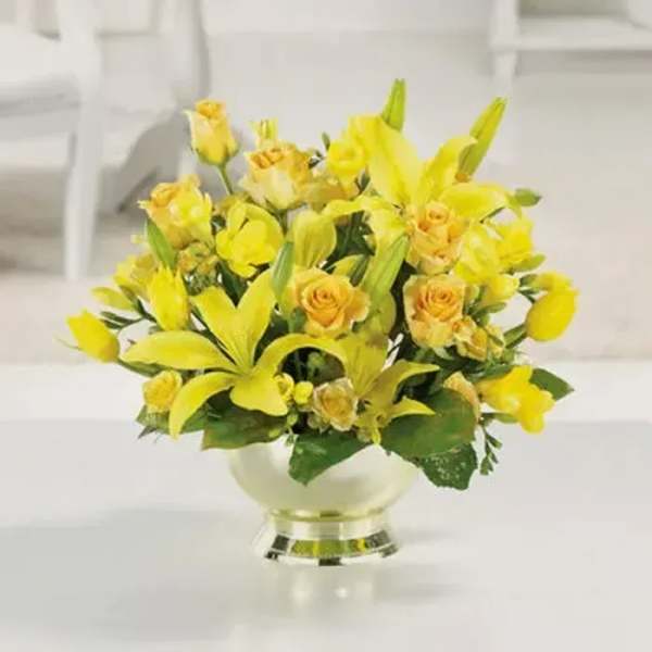 Low arrangement of yellow lilies and roses in a round white pedestal vase