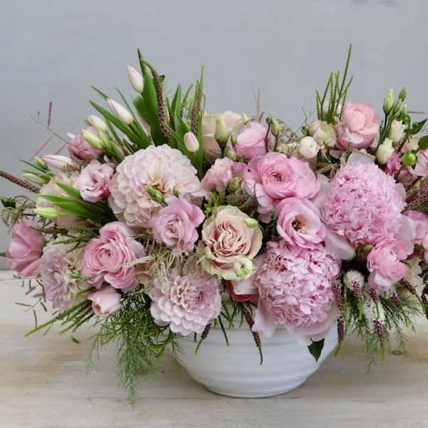 Low pink arrangement of roses, peonies, and other blooms in a white ceramic bowl