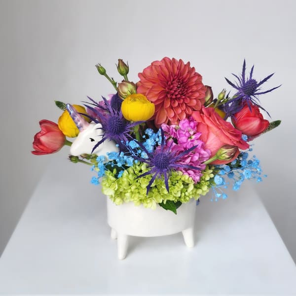 Colorful flower arrangement in a white footed vase with a unicorn accent