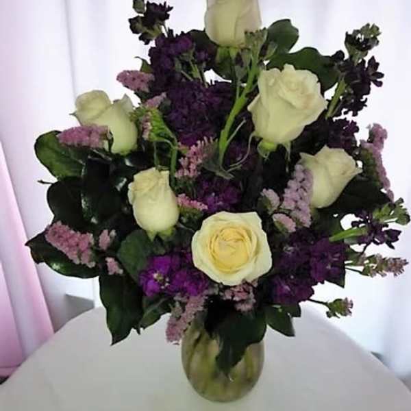 Bouquet of cream roses and purple flowers in a glass vase