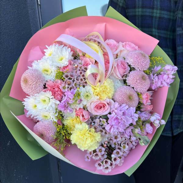 Handheld bouquet of pink, white, and yellow flowers wrapped in pink and green paper