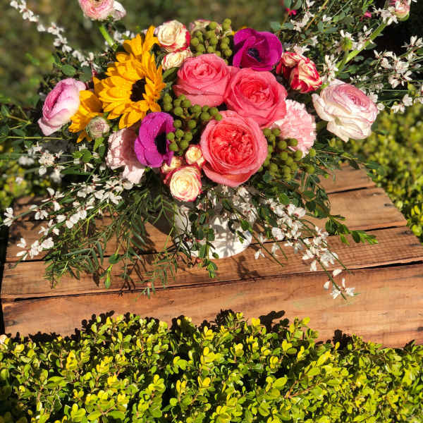 Mixed bouquet with roses, sunflowers, and small white blossoms in a white vase