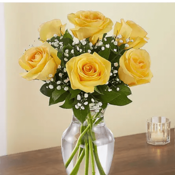 Yellow rose bouquet with baby's breath in a clear glass vase on a wooden table