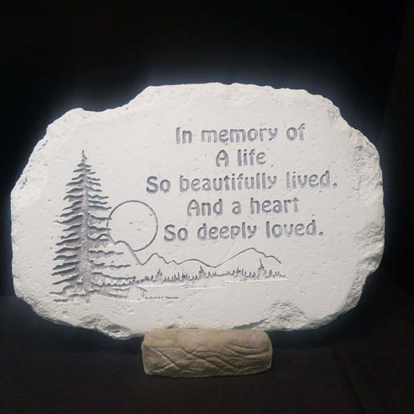 Memorial stone plaque with engraved trees and text on a stand