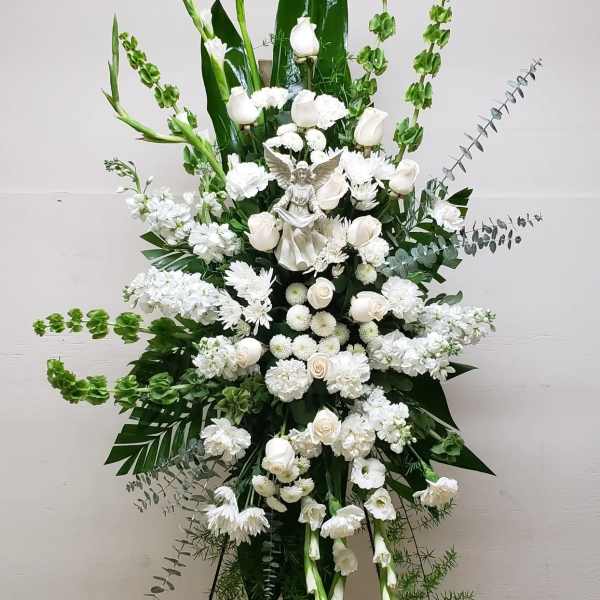 Tall white standing spray with roses, carnations, mums and an angel figurine on an easel