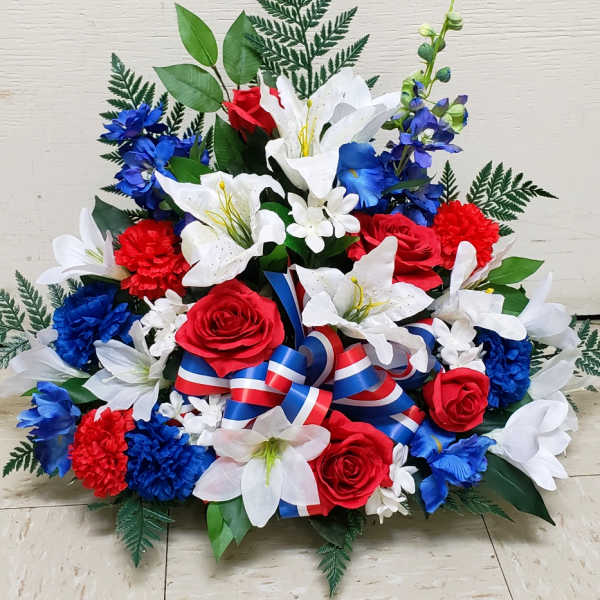 Patriotic arrangement of white lilies, red roses, and blue flowers with a red, white, and blue ribbon