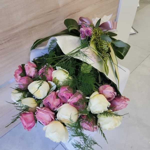 Bouquet of pink and cream roses wrapped in white paper with a satin ribbon bow