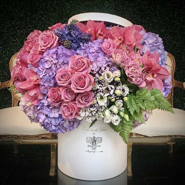 Pink roses and orchids arranged with lavender hydrangeas in a white hatbox
