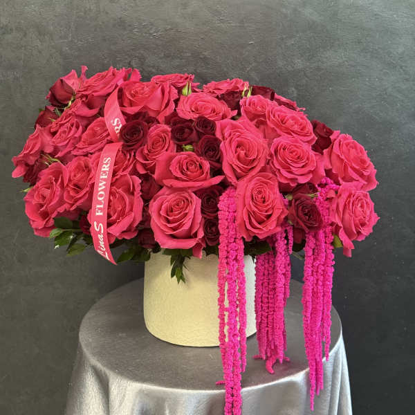 Pink and burgundy roses arranged in a cream hat box with hanging pink amaranthus