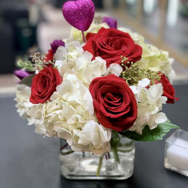 Red roses and white hydrangeas in a glass vase with a pink heart pick